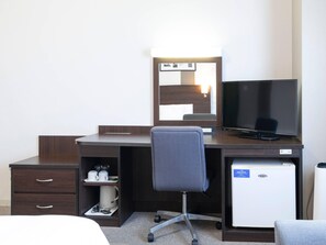 A hotel room with a dark wooden desk, a flat-screen TV, a small refrigerator, a chair, and a bedside table with a lamp. - Comfort Hotel Central International Airport (Tokoname)