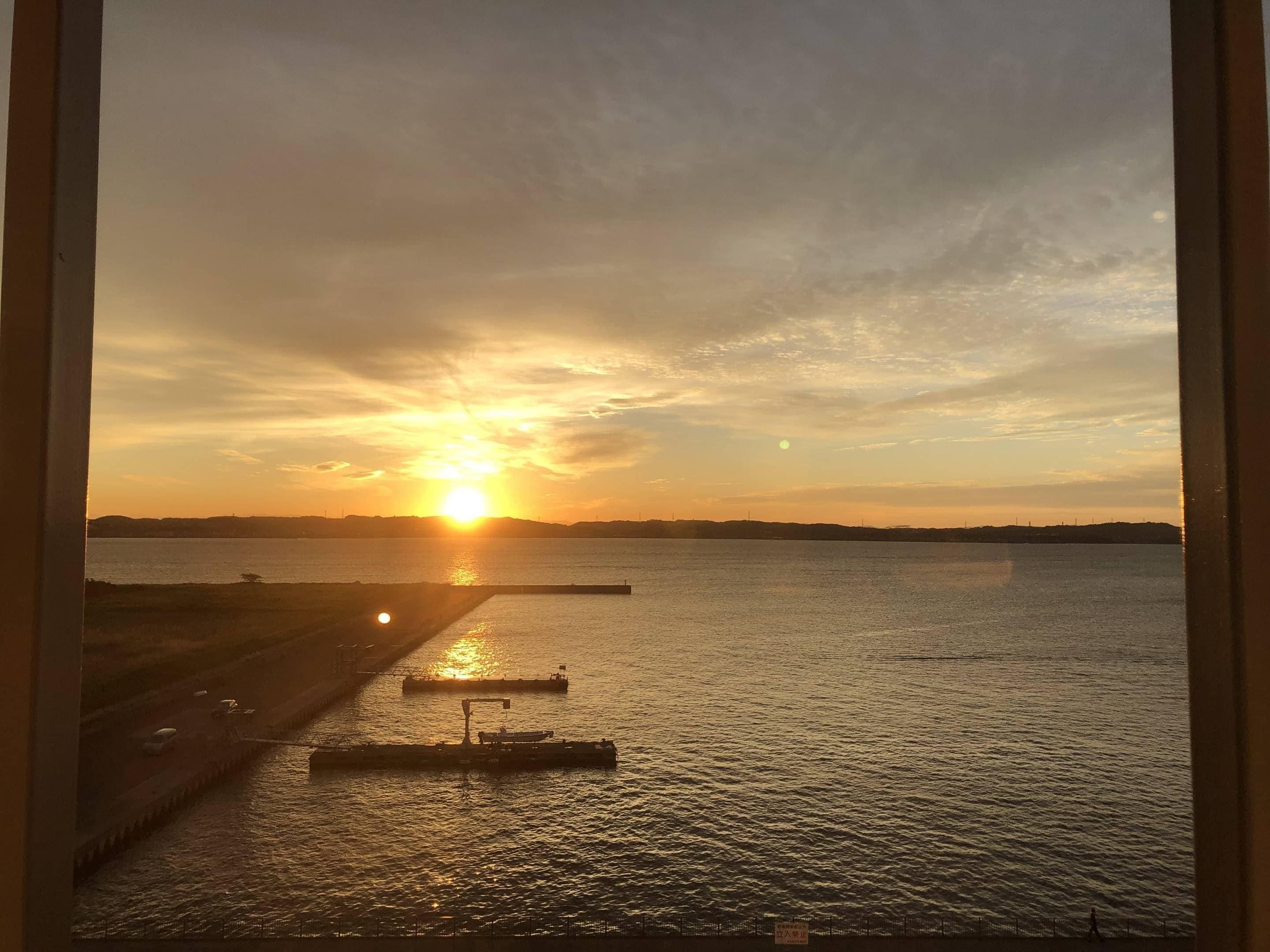 Un atardecer sobre una masa de agua, con un muelle y un puente en primer plano.