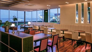 Un moderno vestíbulo de hotel con zona de bar, asientos y ventanas amplias que ofrecen vista a la ciudad y al agua.