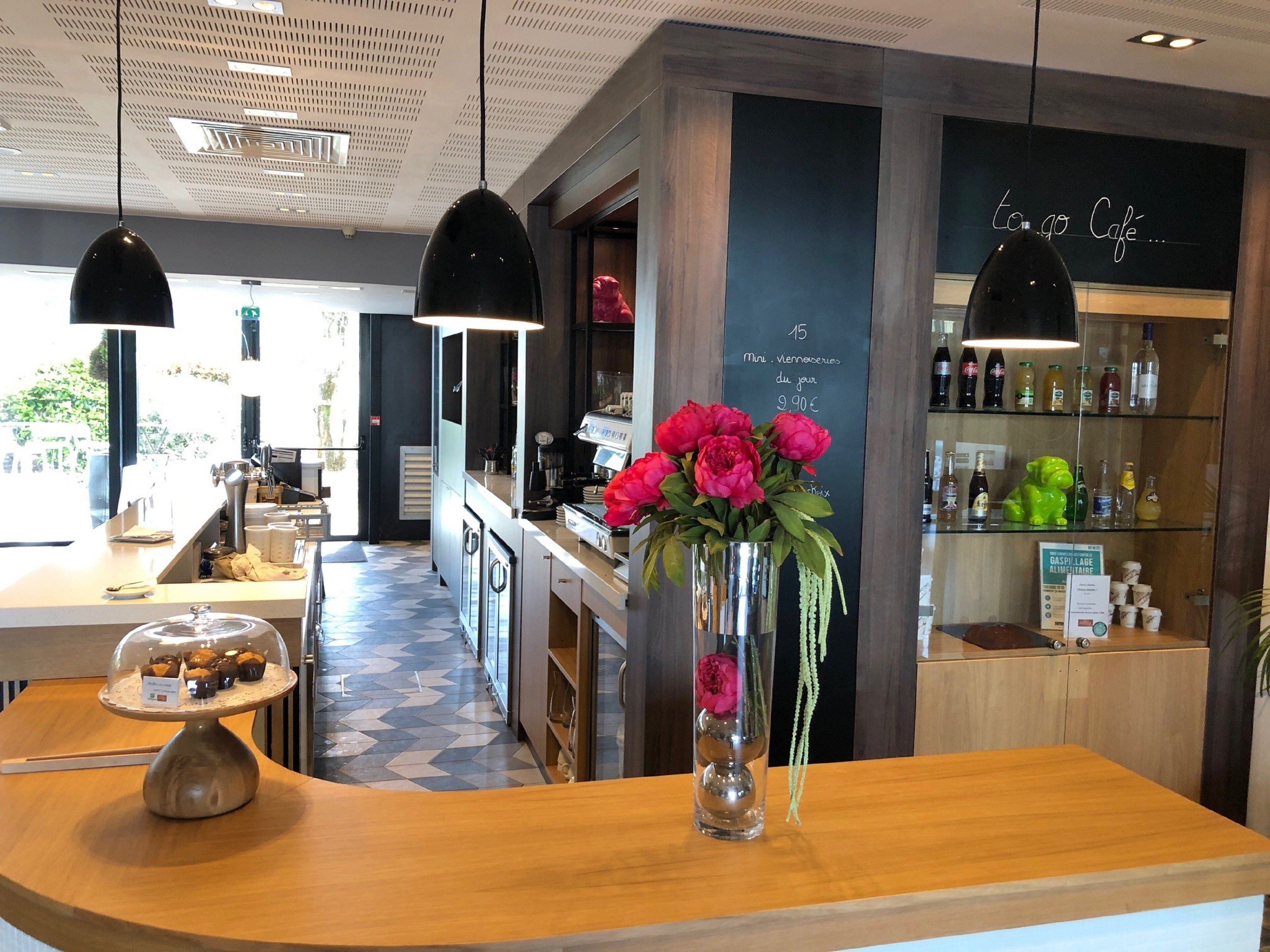 Een café interieur met een houten toonbank, een presentatie van gebak, een vaas met bloemen en een menubord.