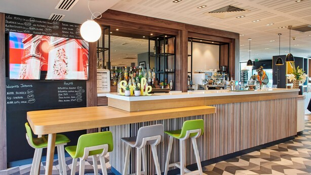 Eine moderne Bar mit einer Holztresen, grünen und weißen Barhocker und einer Tafel mit Getränkeangeboten.