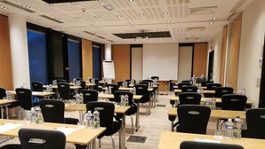 Une salle de conférence avec des rangées de tables et de chaises, équipée de bouteilles d’eau et dotée d’un écran de projection à l’avant.