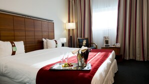 Une chambre d’hôtel avec un lit bien fait, un plateau avec des fruits et une bouteille, un bureau avec un ordinateur portable et une fenêtre avec des rideaux.