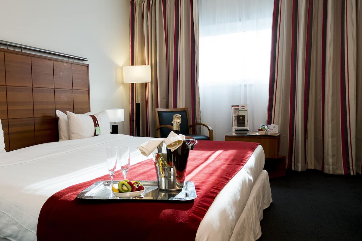 Une chambre d’hôtel avec un lit bien fait, un plateau avec des fruits et une bouteille, un bureau avec un ordinateur portable et une fenêtre avec des rideaux.