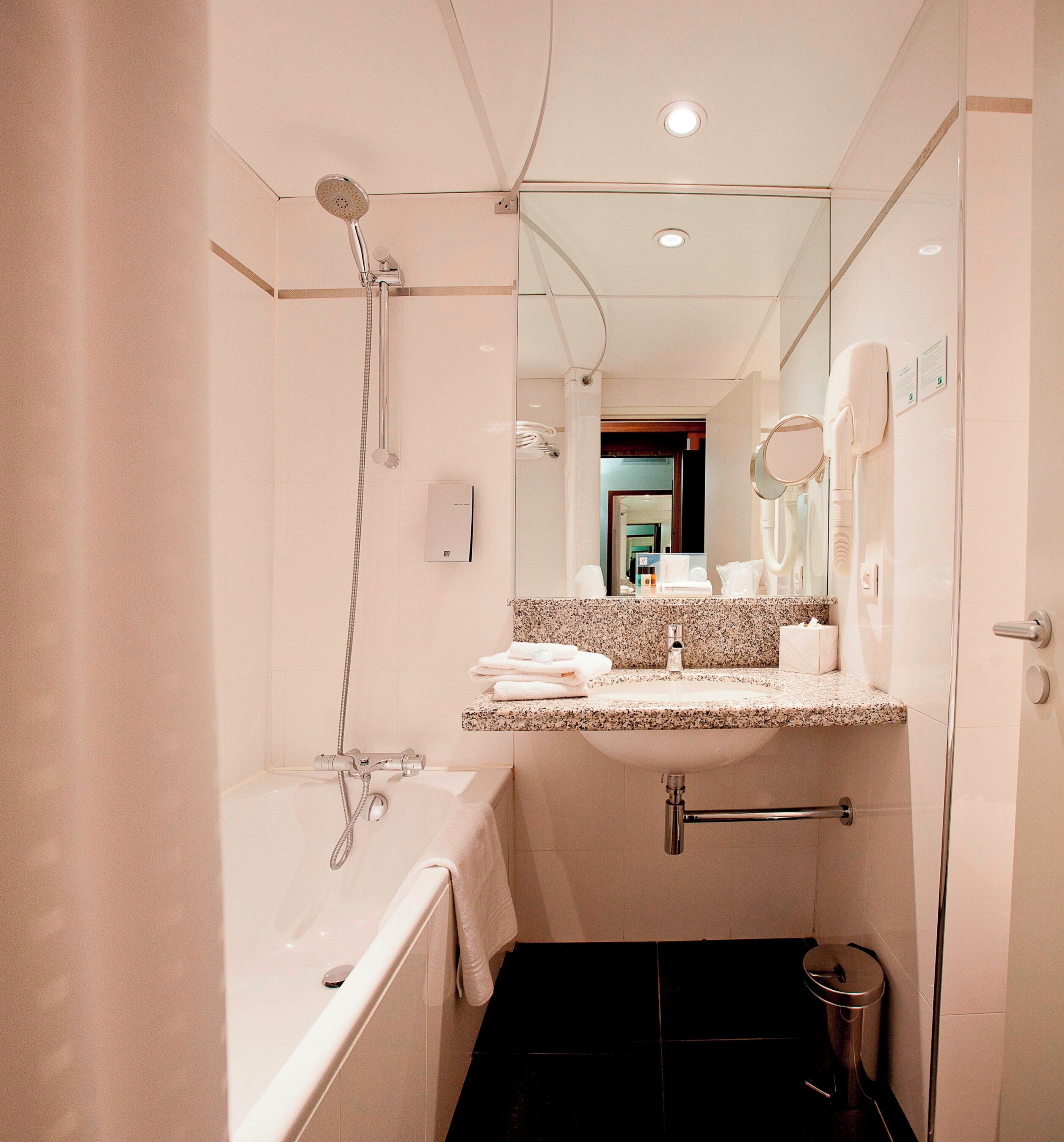 Une salle de bain moderne équipée d’une baignoire, d’une douche, d’un meuble-lavabo avec miroir et de toilettes.