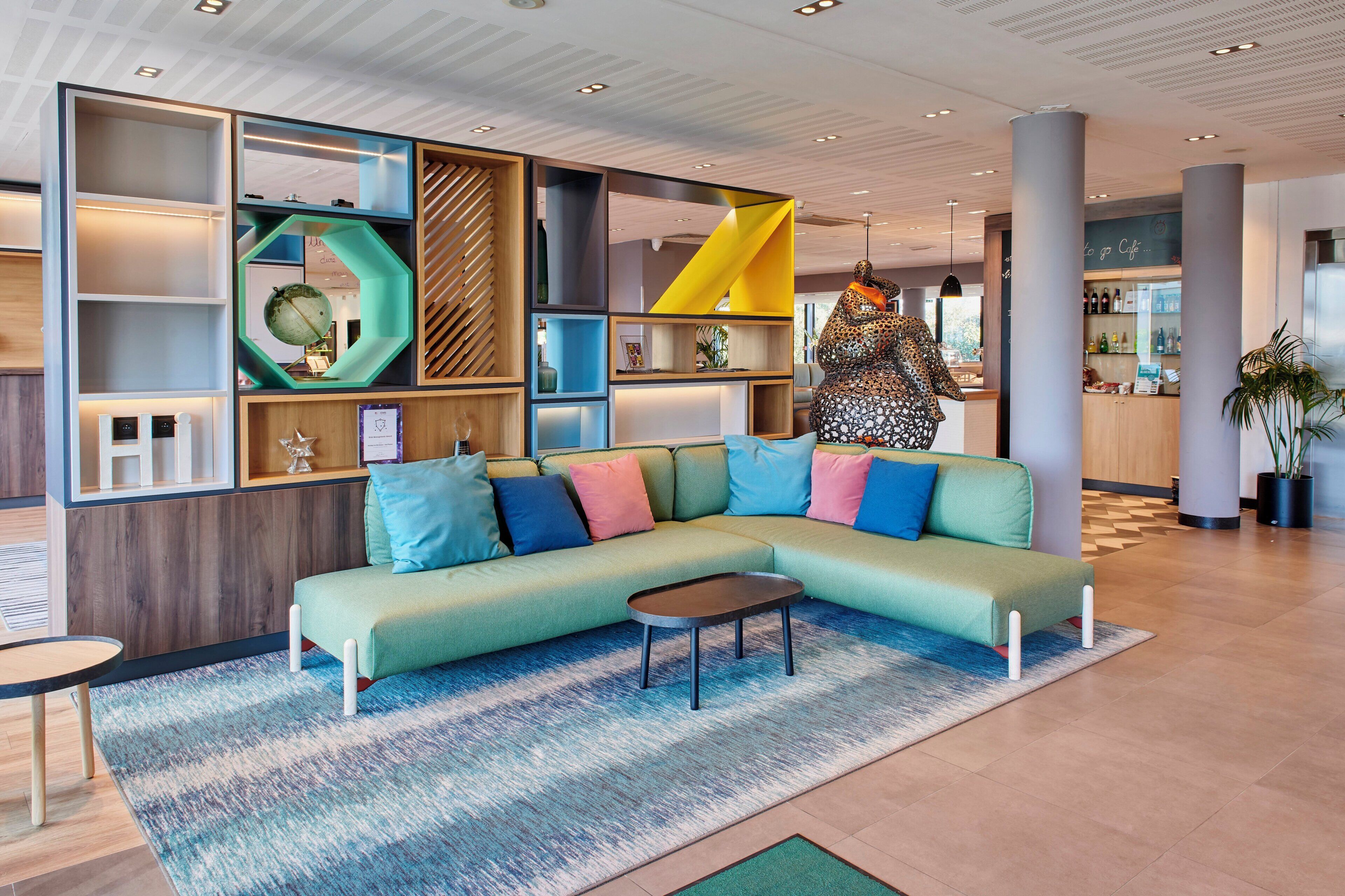 A modern lounge area with a green sectional sofa, a small coffee table, and a patterned rug.