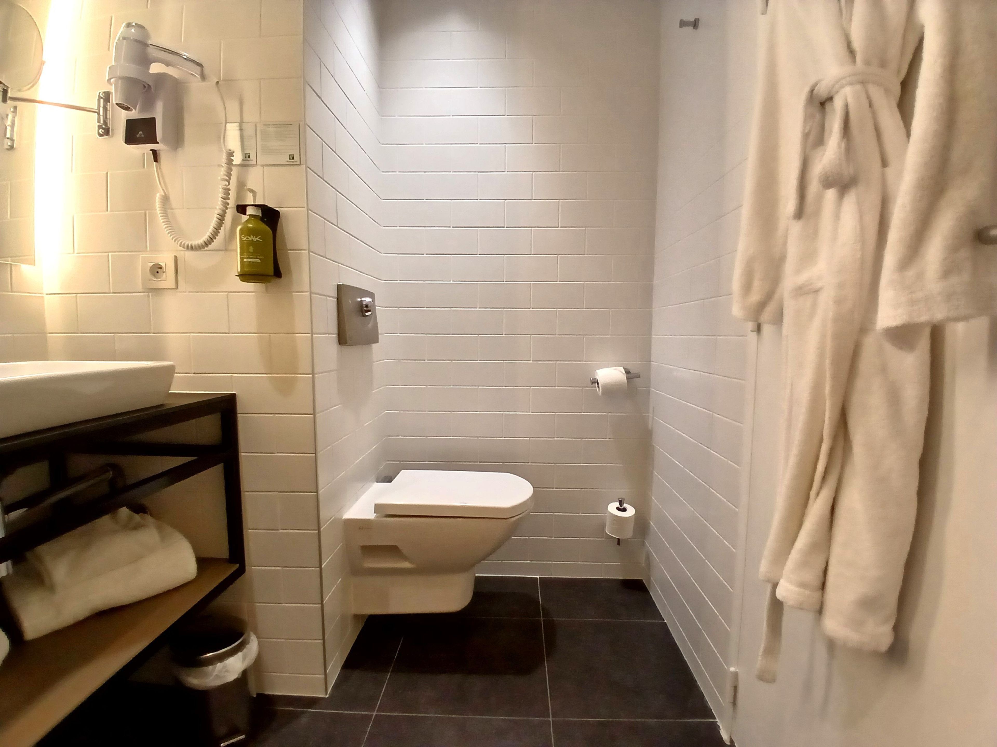 A bathroom with a toilet, sink, and a hairdryer mounted on the wall.