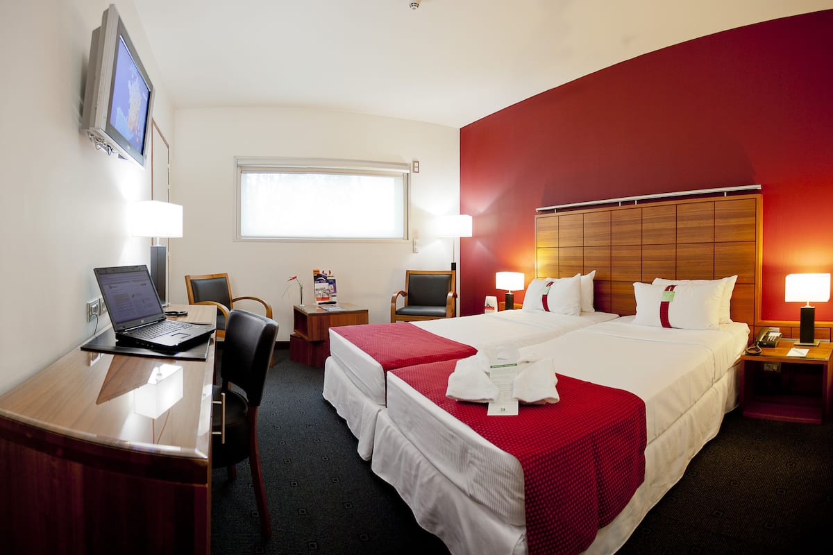 Une chambre d’hôtel avec un bureau, deux lits, une télévision et une fenêtre.