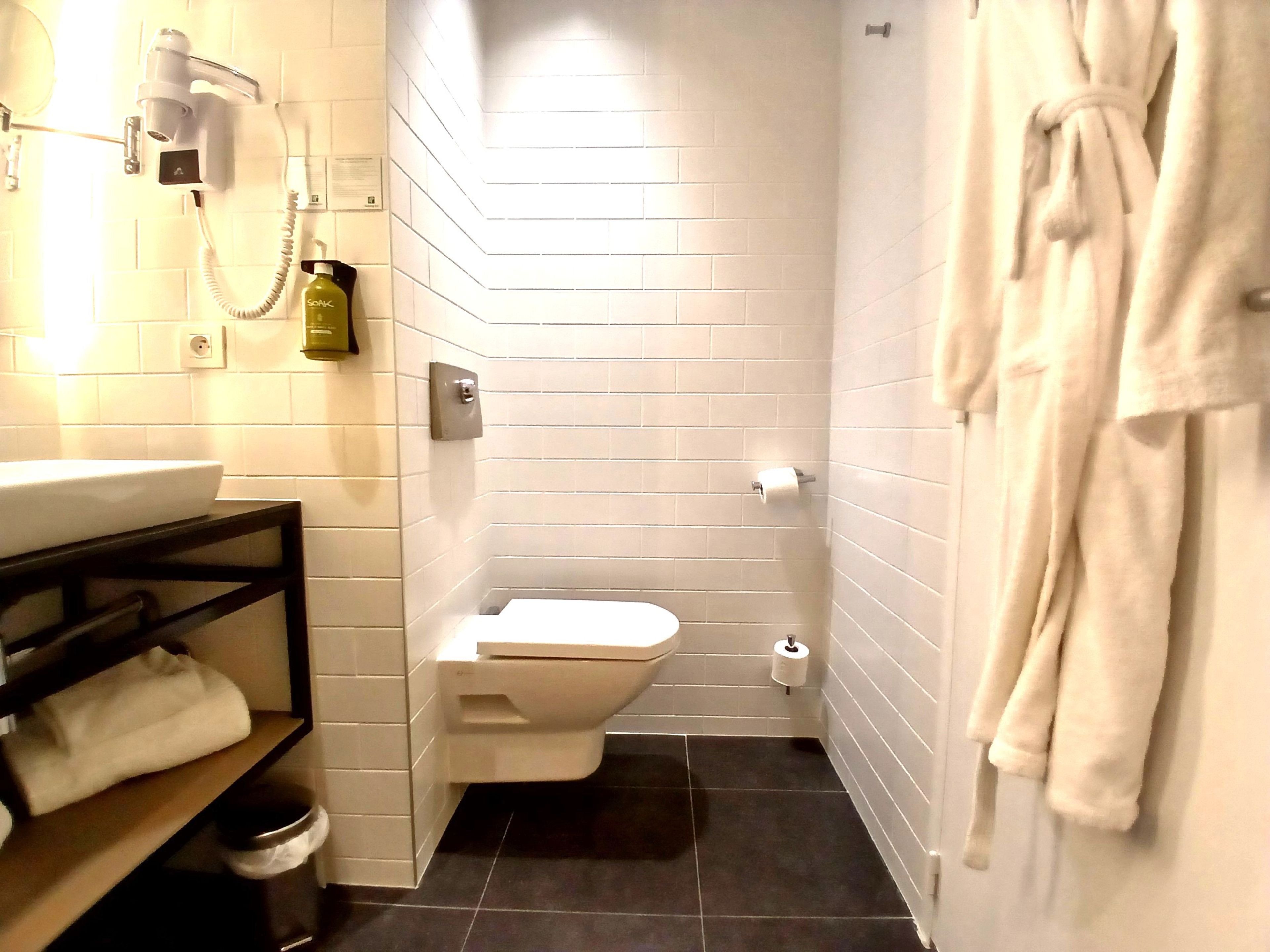 Un baño con inodoro, lavamanos, toallero y un secador de pelo en la pared.