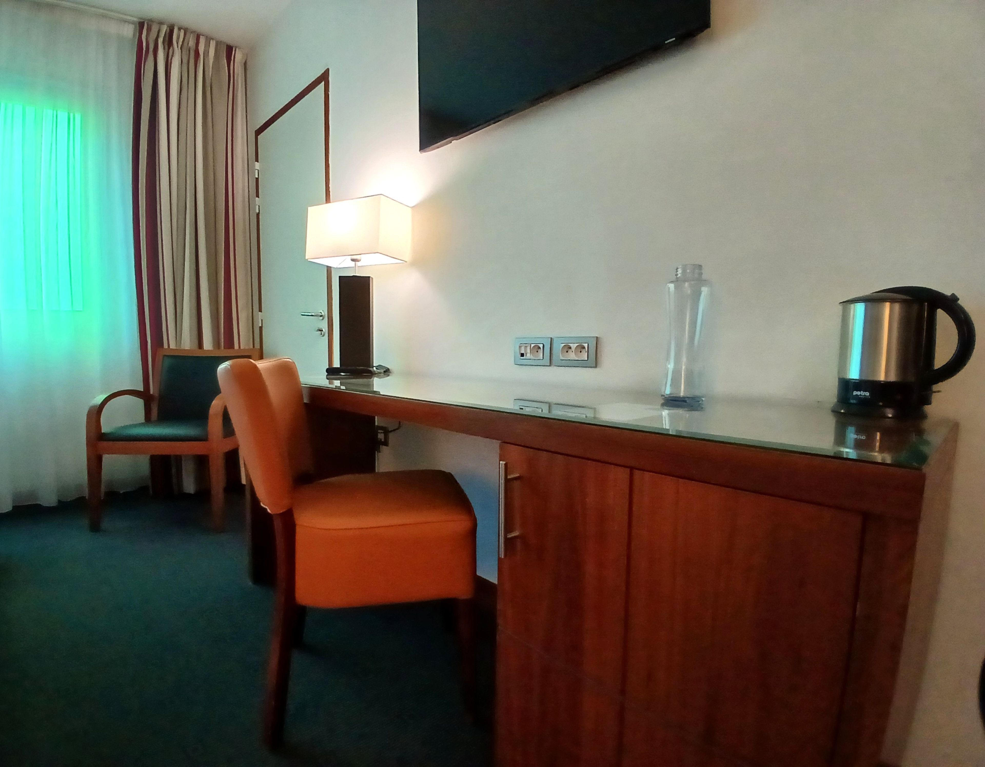Une chambre d’hôtel avec un bureau en bois, une chaise, un téléviseur fixé au mur et une lampe.