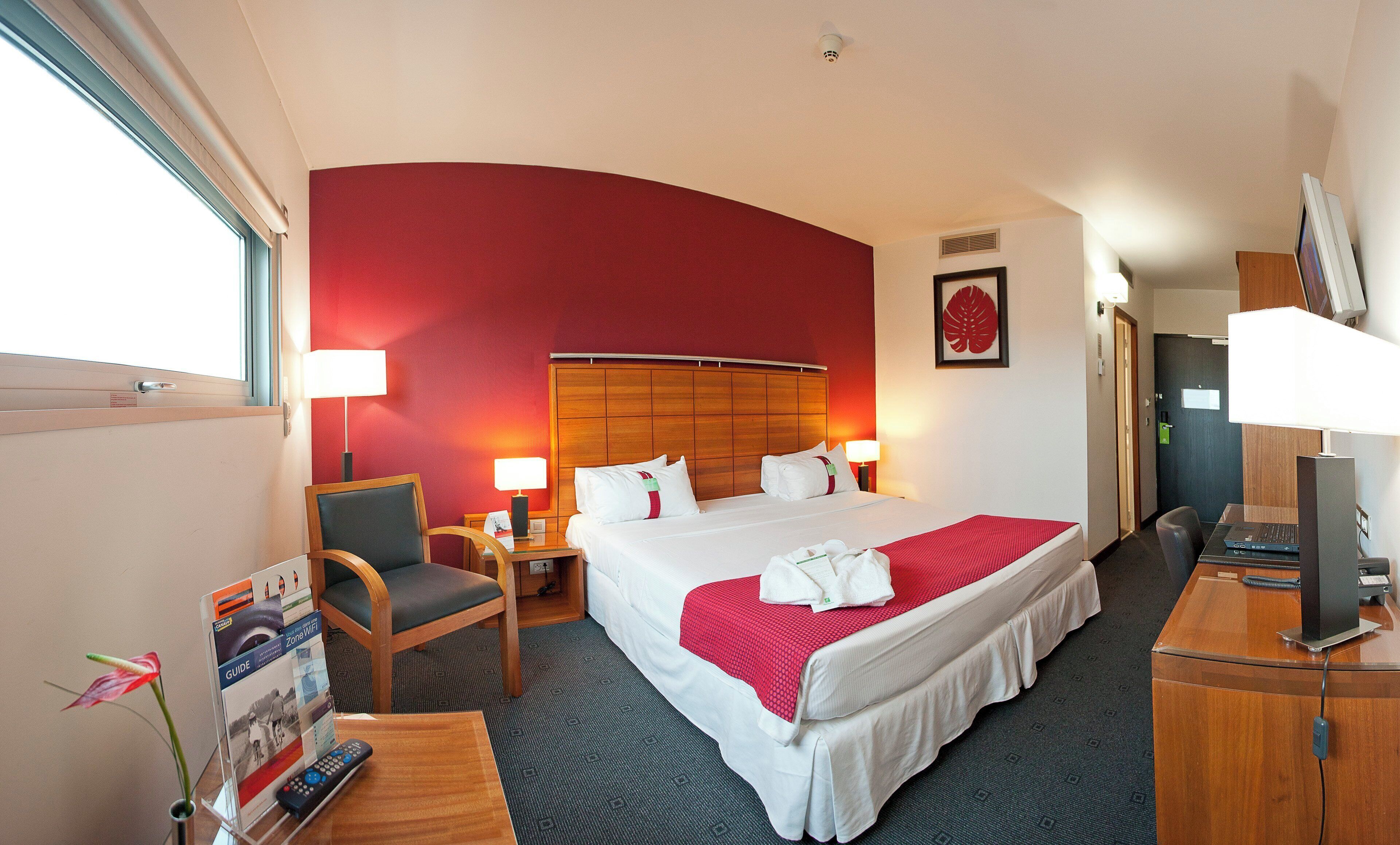 Una habitación de hotel con cama, escritorio, silla y lámpara de escritorio.