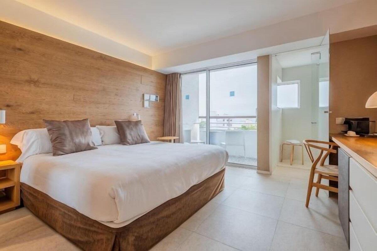 Habitación de hotel con una cama grande, un escritorio, una silla, un balcón y una pared de madera.