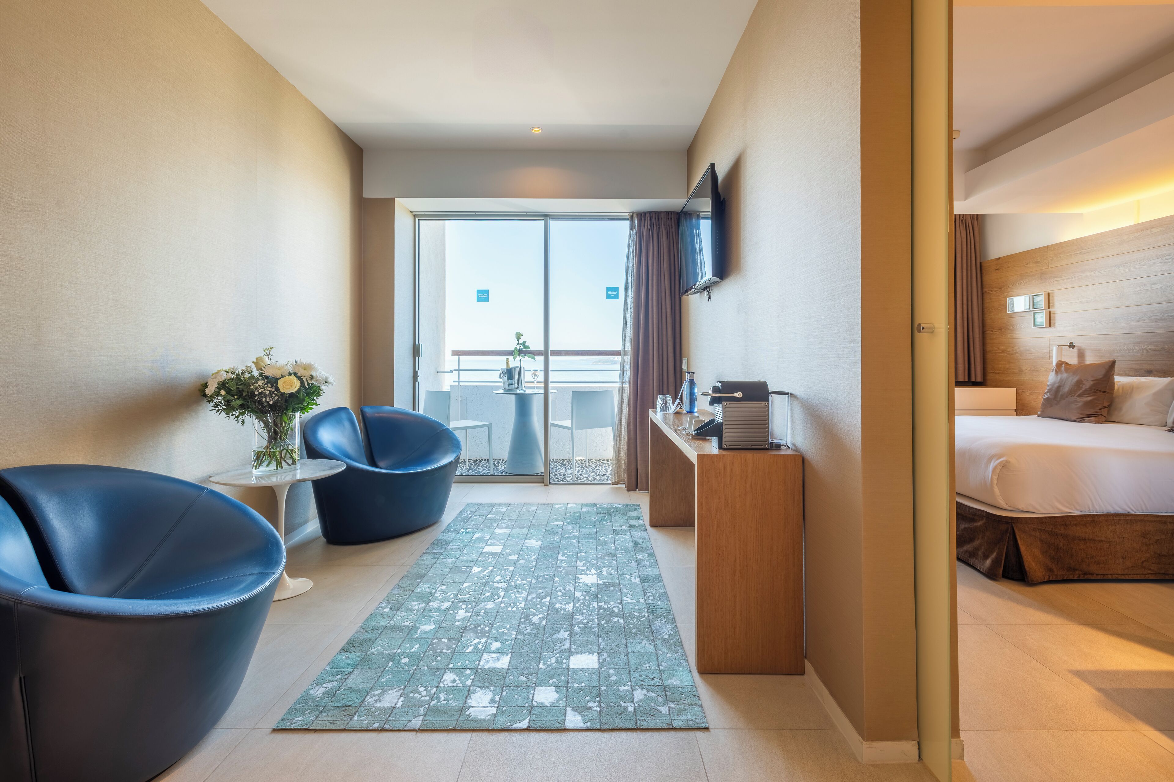 Habitación de hotel con cama, escritorio, televisor y vistas al balcón exterior.