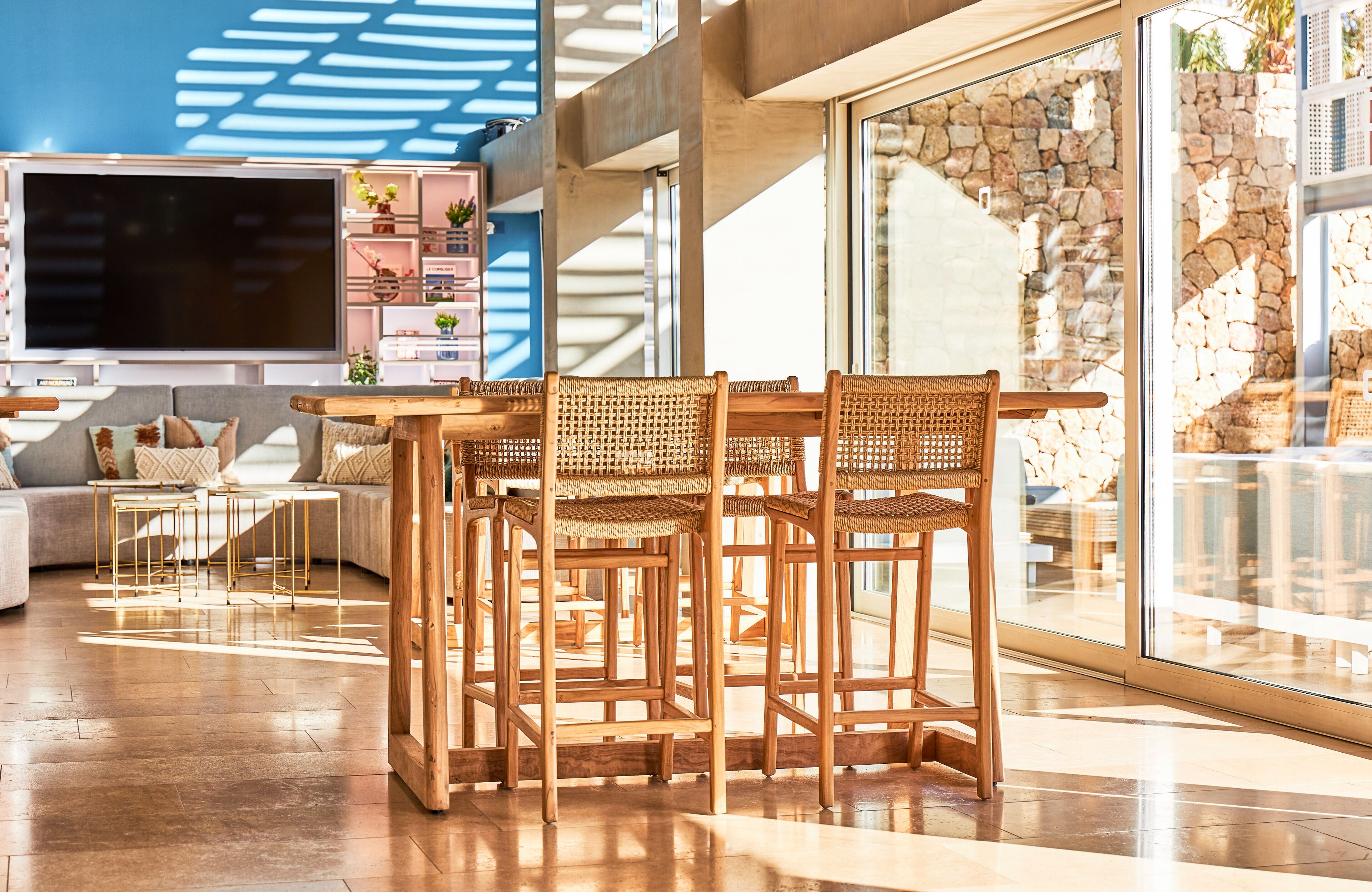 Un salón moderno con un televisor de pantalla plana grande, sillas de mimbre, una mesa de centro de madera y una pared de piedra.
