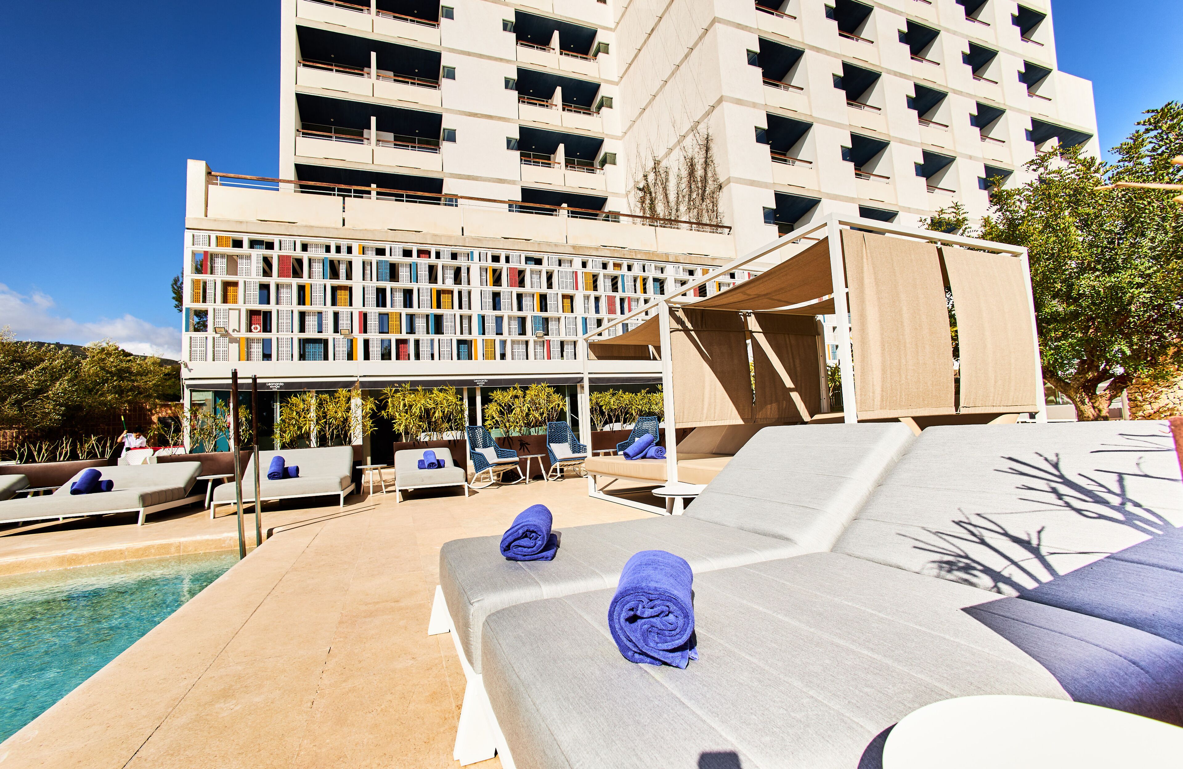 A poolside area with lounge chairs and a building with a unique facade in the background.