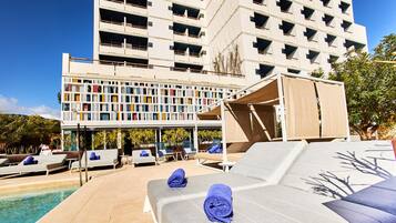 Zona piscina con lettini e un edificio dallo stile architettonico distintivo sullo sfondo.