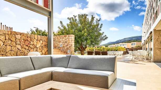 Un área de estar moderna al aire libre con un muro de piedra, un árbol grande y vistas de edificios al fondo.