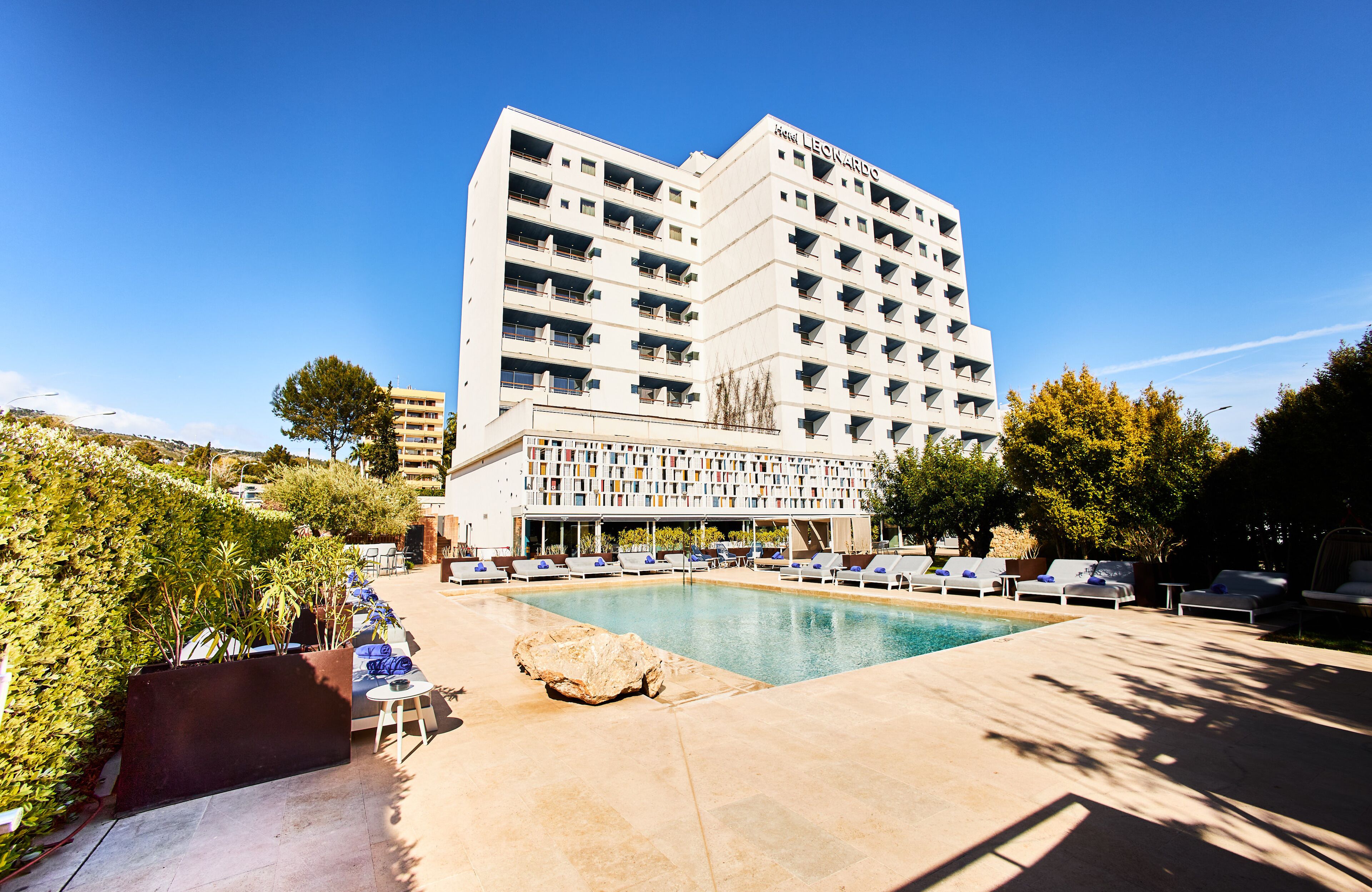 A hotel with a pool area, lounge chairs, and a large building with balconies.