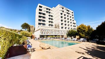 A hotel with a pool area, lounge chairs, and a large building with balconies.