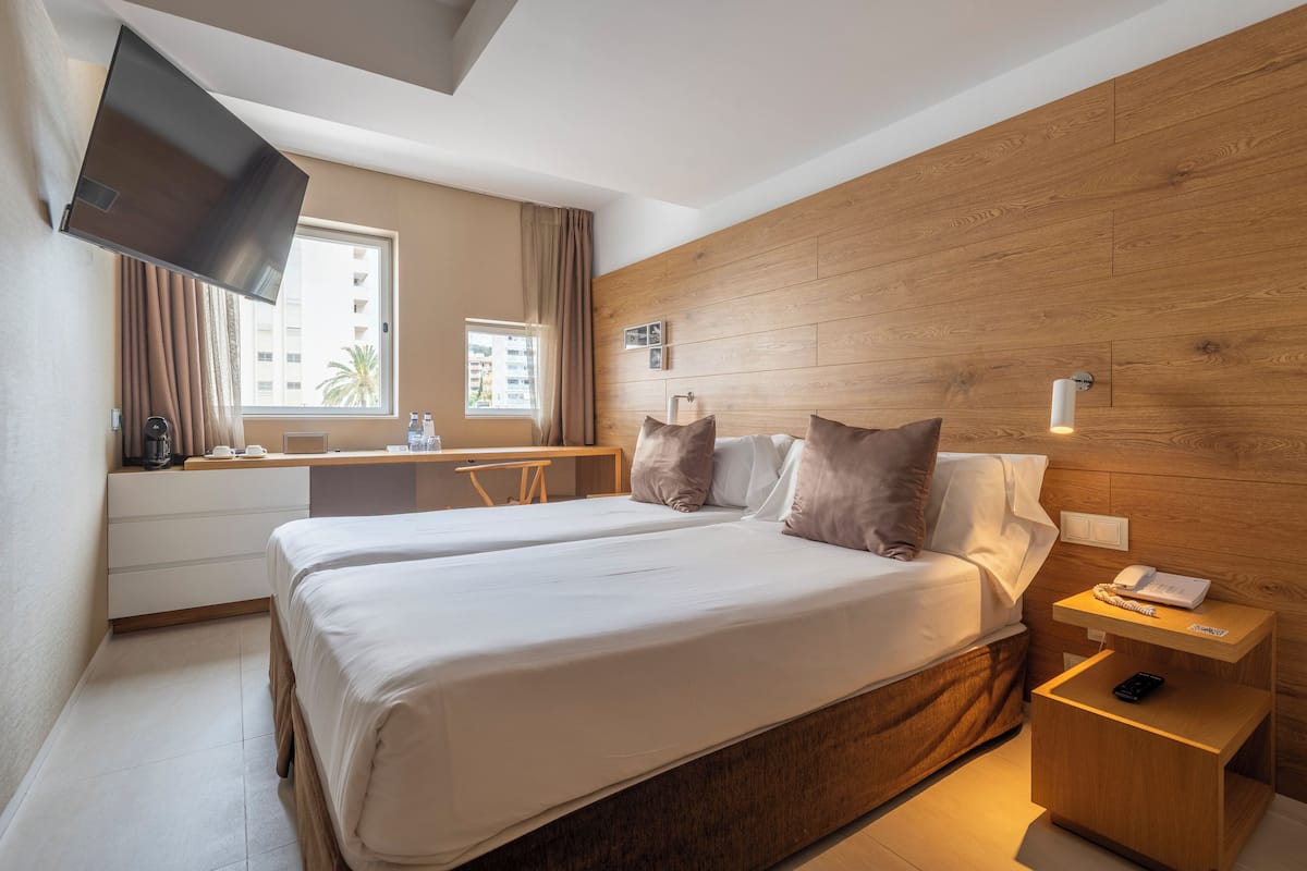 A hotel room with a large bed, a desk with a chair, a TV mounted on the wall, and a wooden headboard.
