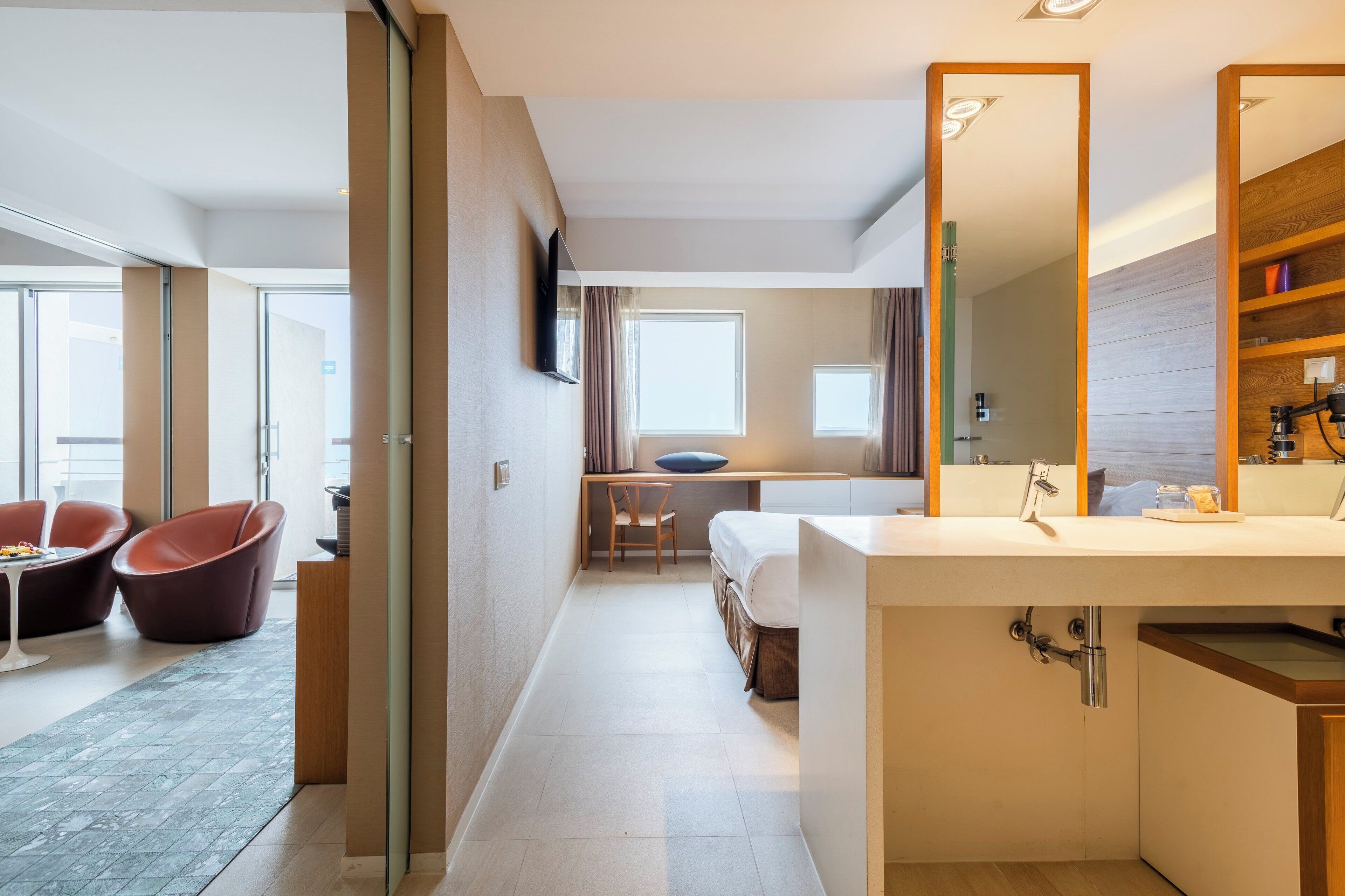 Habitación de hotel moderna con un espejo grande, un escritorio, una cama y una zona de estar con sillas.