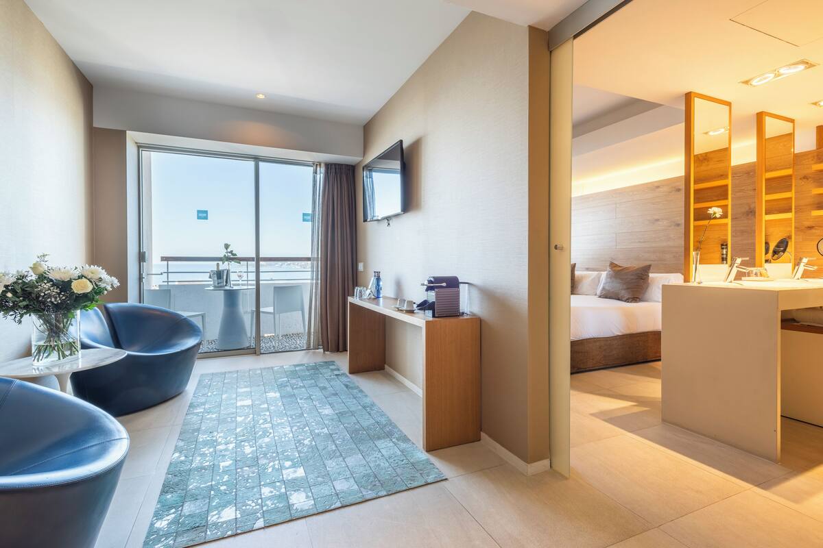 A modern hotel room with a balcony, a desk, a bed, and a TV.