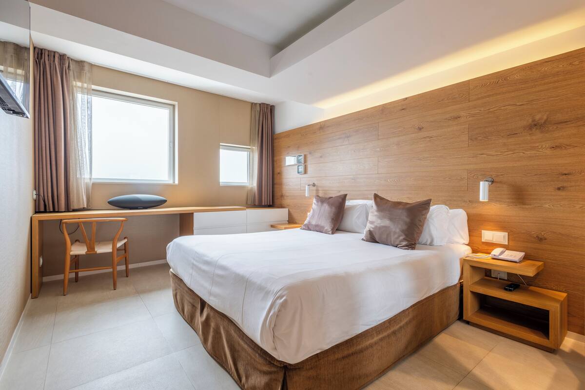 A modern hotel room with a large bed, a desk, and a computer.