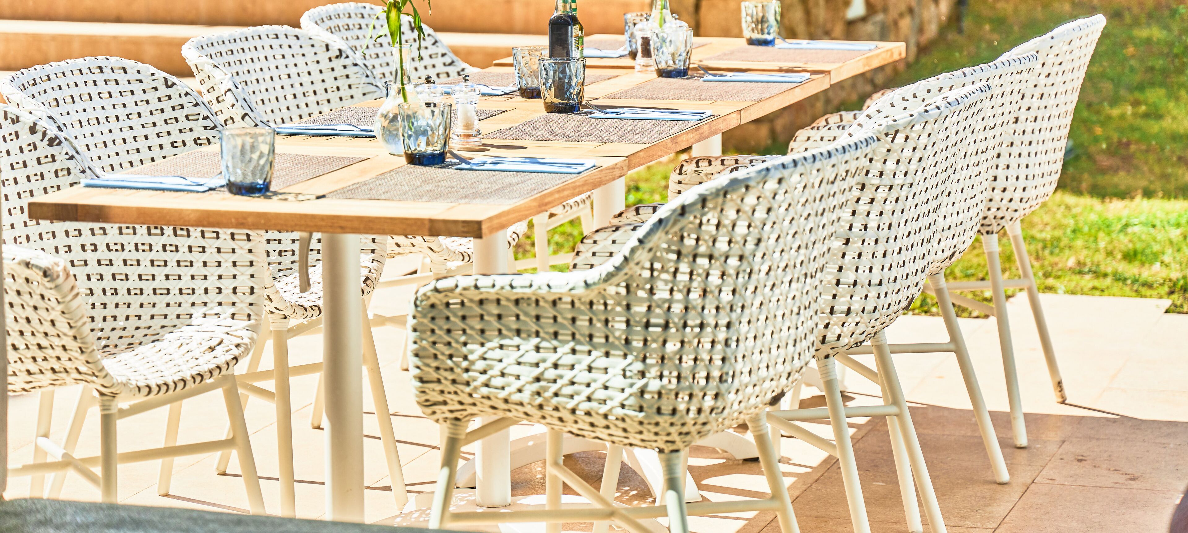 Un comedor con una larga mesa de madera, sillas de mimbre y vasos de vidrio transparente.