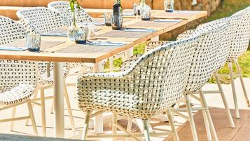 Un comedor con una larga mesa de madera, sillas de mimbre y vasos de vidrio transparente.