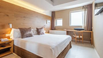 Een moderne hotelkamer met een groot bed, een houten hoofdeinde, nachtkastje en een bureau met stoel.