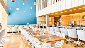 Un comedor moderno con mesas largas, sillas blancas y una pared azul con luces circulares.
