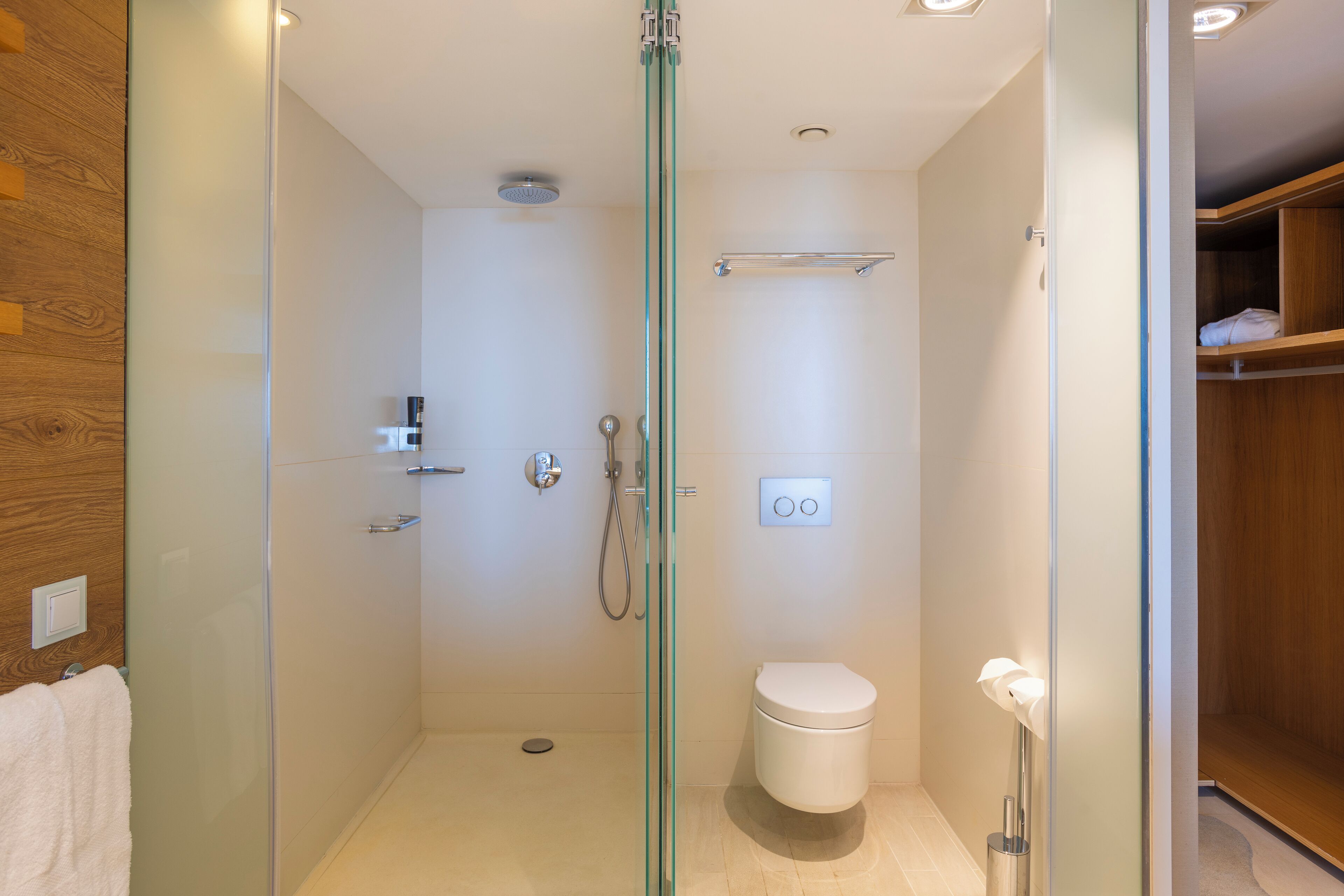 Un baño moderno con ducha de vidrio, inodoro y tocador de madera con perchero.