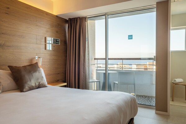 Habitación de hotel con una cama grande, una pared de madera, un balcón con vistas y una pequeña mesa con una toalla.