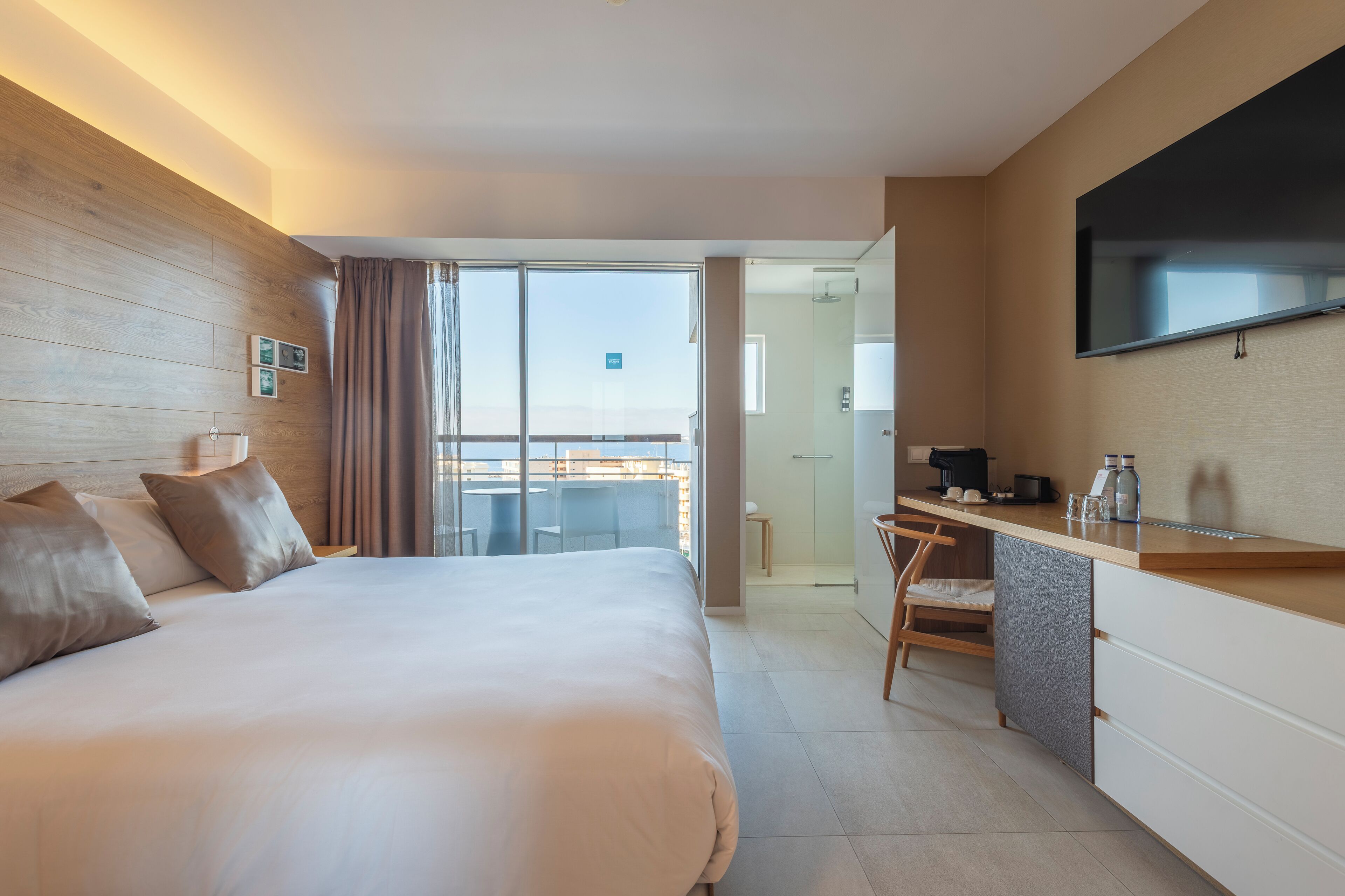 A modern hotel room with a large bed, a desk, a flat-screen TV, and a balcony with a city view.