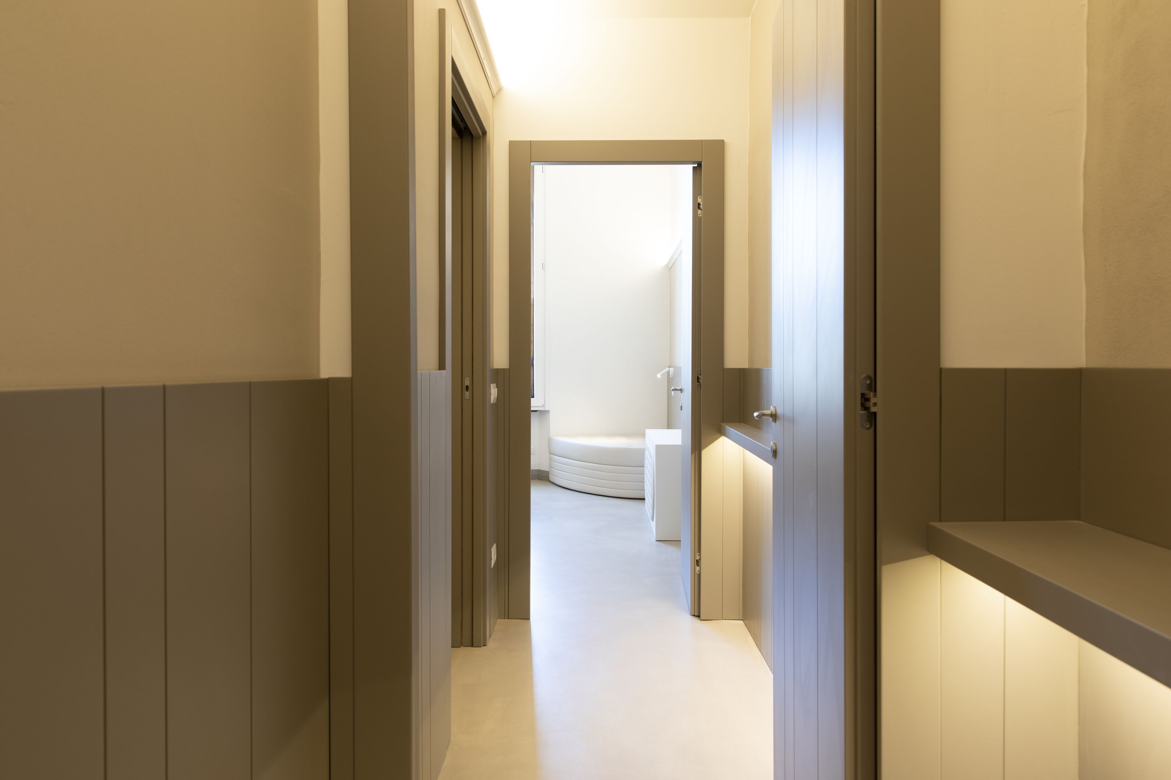 Un estrecho pasillo con paneles de madera y suelo blanco que conduce a un baño con bañera y retrete.