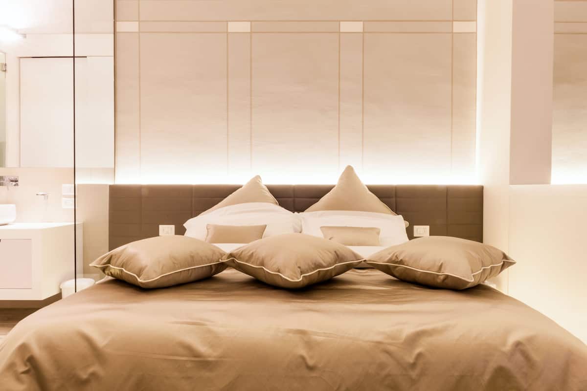 Ein modernes Schlafzimmer mit einem großen Bett, einem Kopfteil mit vertikalen Paneelen und einem Nachttisch mit einer Lampe.