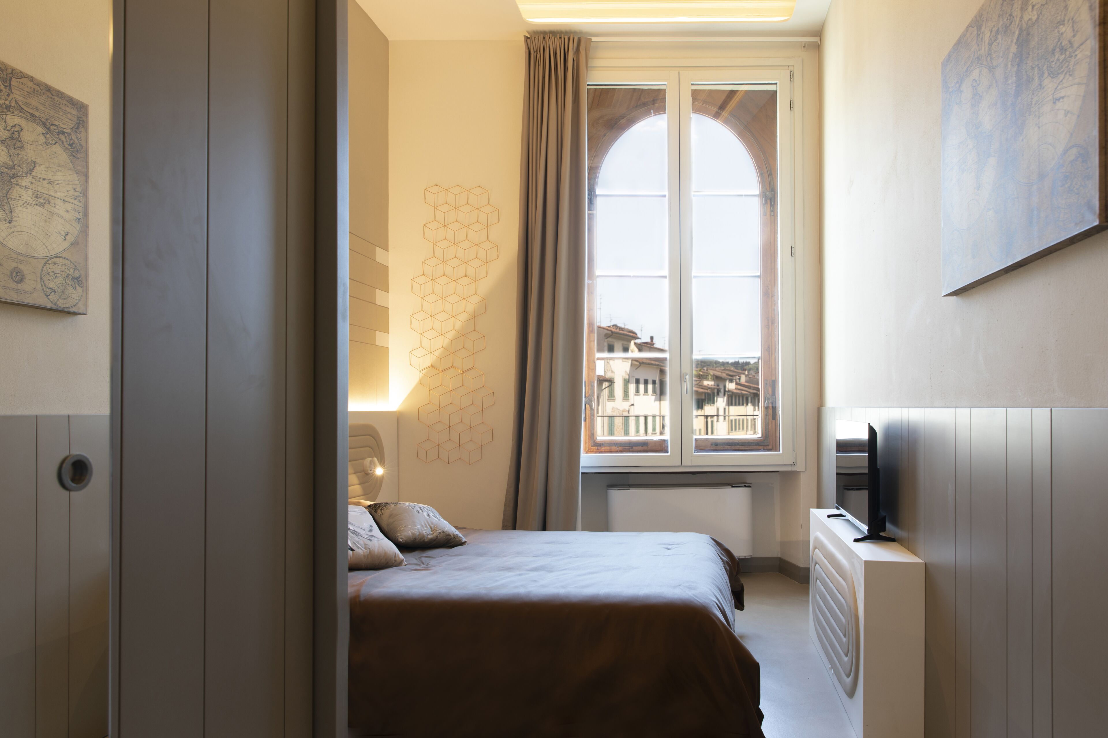 A bedroom with a bed, a radiator, a TV, and a window with a view of buildings.
