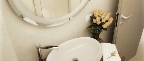 A bathroom with a round mirror, a sink, and a vase with flowers.