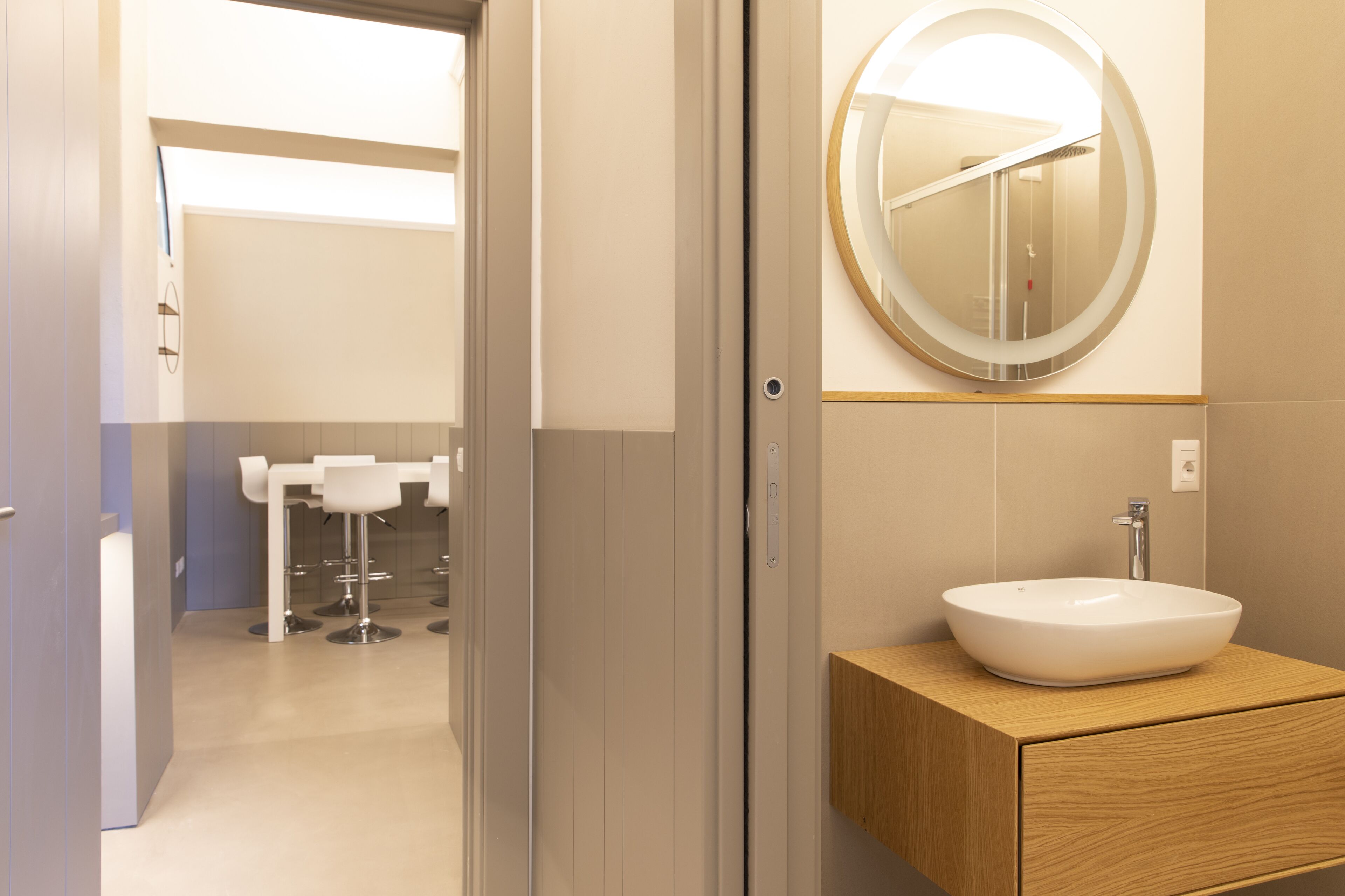 A modern bathroom with a large oval mirror, a wooden vanity, and a white sink.