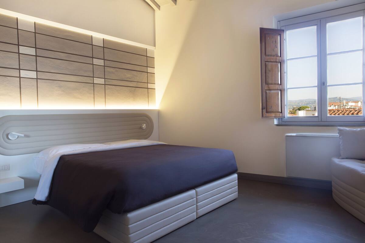 Ein Schlafzimmer mit Bett, Nachttisch, Fenster mit Blick und einem Kopfteil mit Lichtleiste.