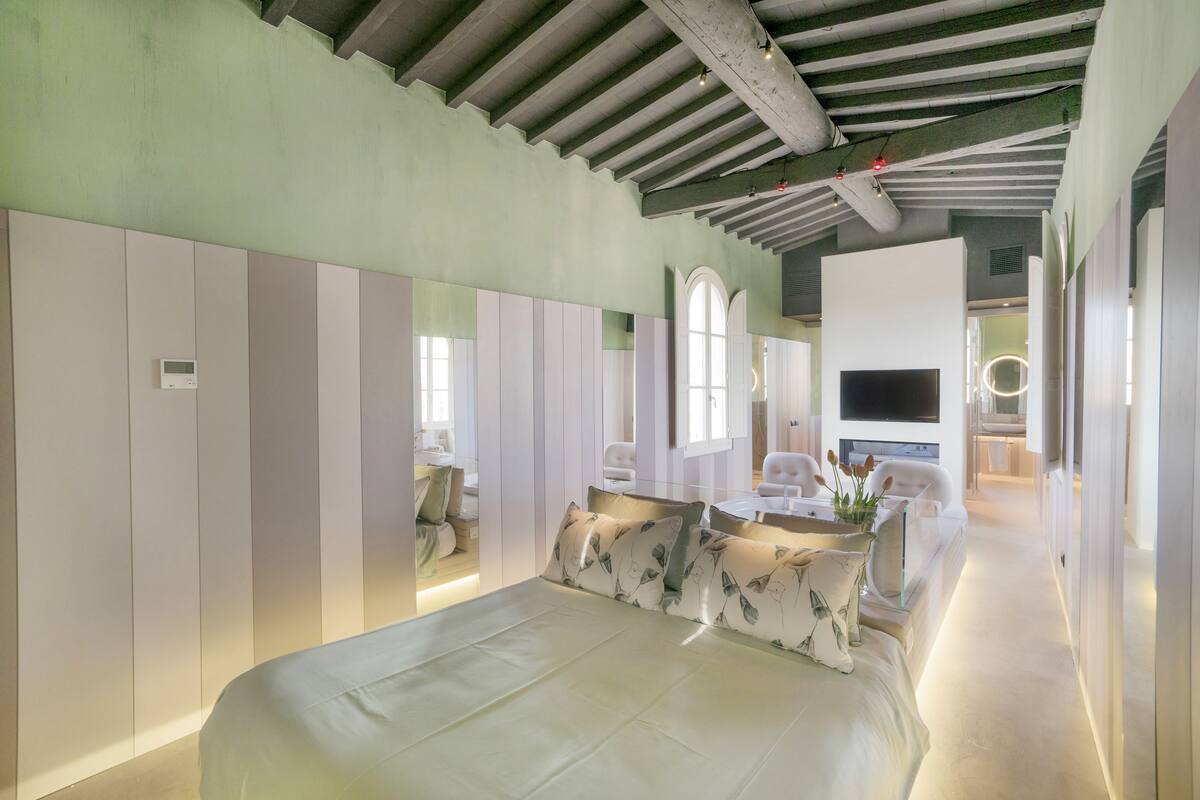 Ein modernes Hotelzimmer mit einem großen Bett, einem Schreibtisch mit Stuhl, einem Fernseher und einer Sitzecke mit Sofa und Sesseln.