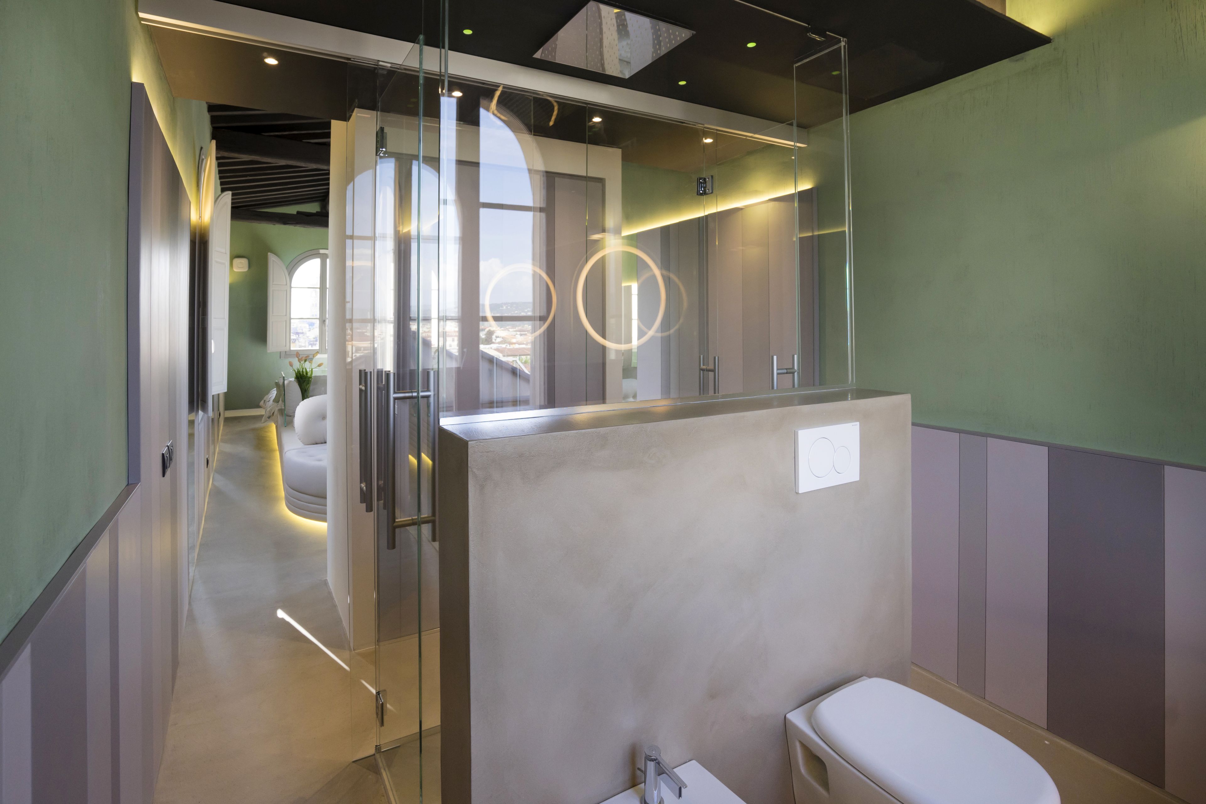 A modern bathroom with a glass partition, a white toilet, and a view of the city through the window.