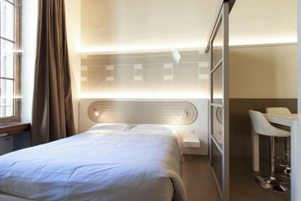 Una habitación de hotel con cama, mesita de noche y escritorio con sillas.