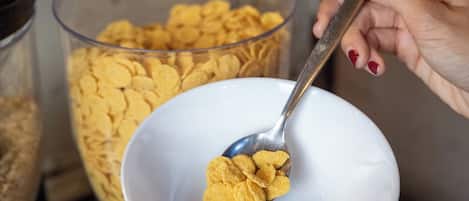 A person scooping cereal from a large container into a bowl.