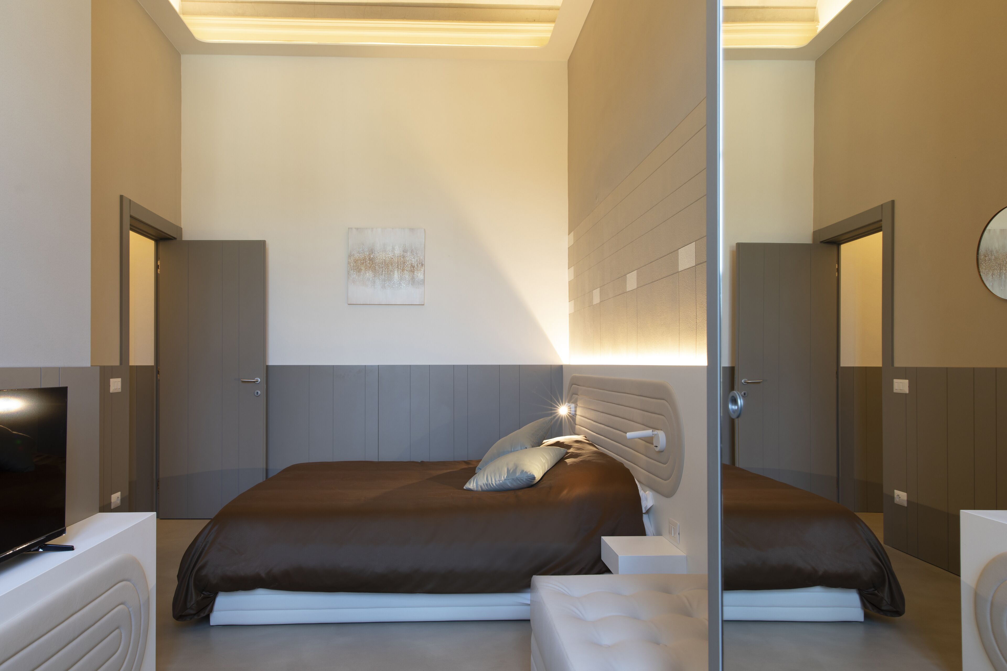 Une chambre à coucher moderne avec un grand lit, une télévision et un miroir.