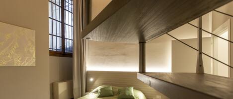 A modern bedroom with a bed, a nightstand, a window, and a wall-mounted light fixture.