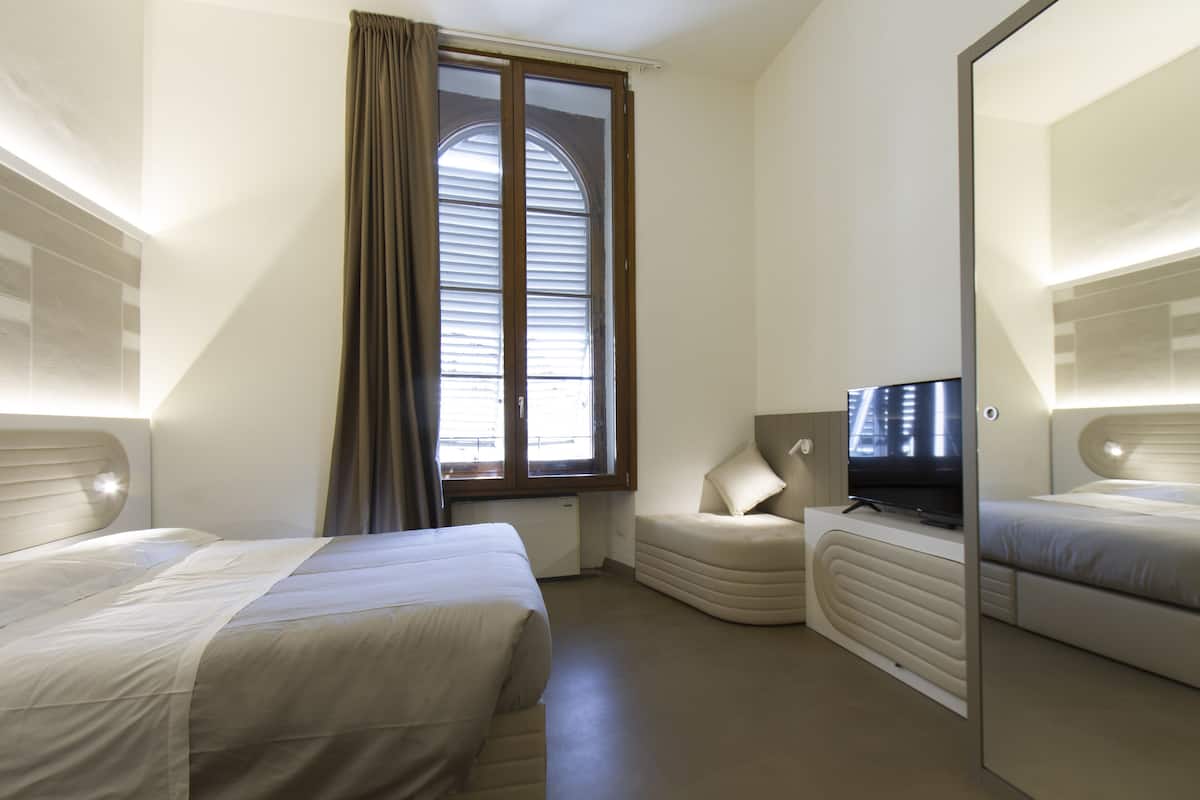 Ein Hotelzimmer mit zwei Betten, einem Fernseher, einem Schreibtisch und einem Fenster mit Vorhängen.
