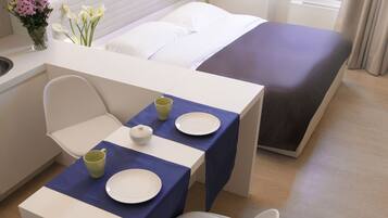 Una habitación de hotel moderna con una cama, un escritorio pequeño con una silla, una mesa con platos y tazas, y un jarrón con flores.