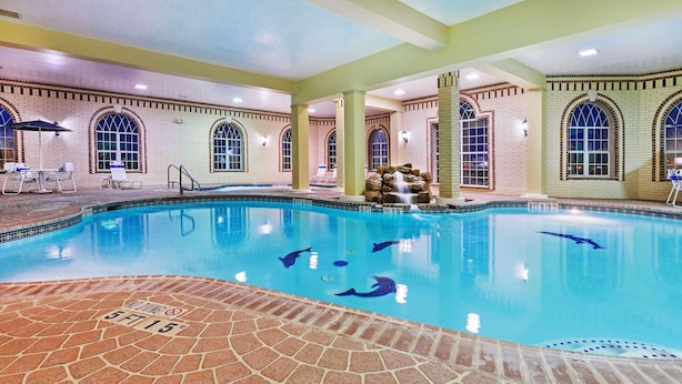 A swimming pool with clear water, a brick deck, and a waterfall feature.