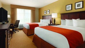 A hotel room with two beds, a desk with a computer, a chair, and a window with curtains.